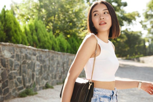 Summer sunny lifestyle fashion portrait of young stylish hipster Asia woman walking on the street, wearing cute trendy outfit, turn behind and looking thoughtful.